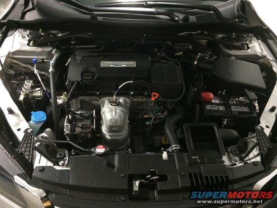 Engine bay of a silver car, showing the engine, battery, and various hoses. The car has a 2013 model year