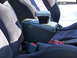 1993 Mazda MX-3 - Interior view of a car's center console armrest and dark fabric seats, with a red cloth visible beneath the armrest.