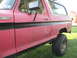 1979 Ford Bronco - The side of a red 1979 Ford Bronco Ranger with a black stripe and visible rust damage.