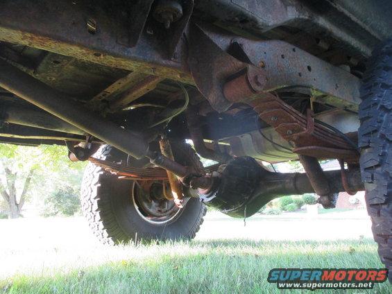 Undercarriage view showing leaf springs, differential, and exhaust pipe of an older vehicle