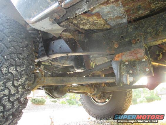 Underside view of a 4x4 vehicle's frame, suspension, and tires. Shows significant rust