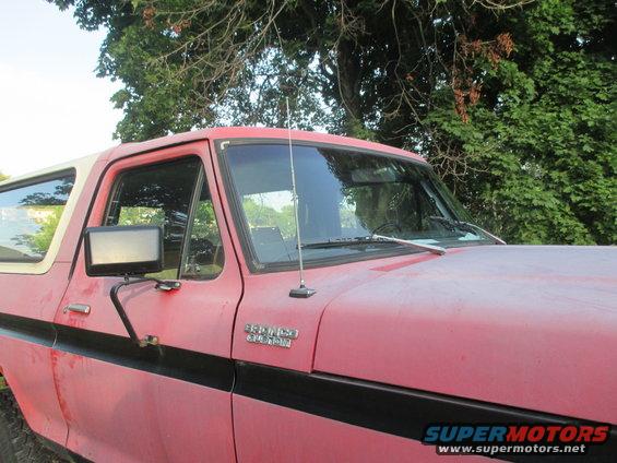 Red Ford Bronco with a white top, black stripe, and side mirror. The vehicle appears weathered