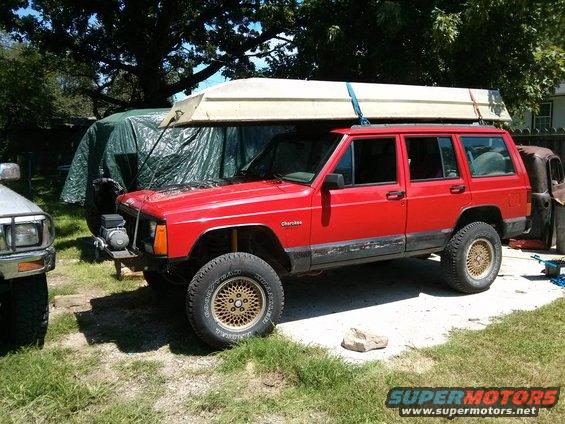 Red Jeep Cherokee side view with boat on roof rack