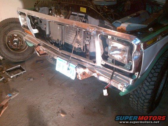 Truck front end with grille removed, showing radiator and headlights. License plate is visible