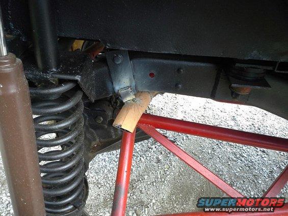 Close-up of a vehicle's suspension with a red roll cage visible. Shows a shock absorber, coil spring, and frame components