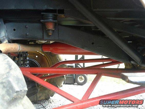 Undercarriage with red suspension components and large tire. A utility vehicle is visible in the background
