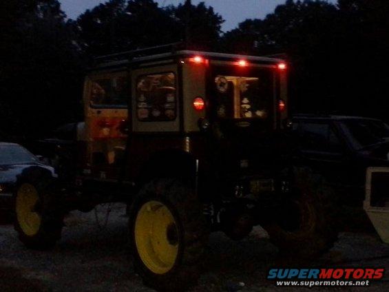 Off-road vehicle with yellow wheels and roof rack, parked next to another vehicle at dusk