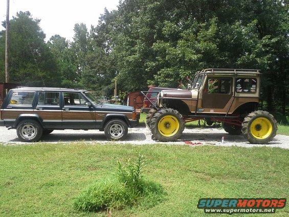Custom lifted Jeep with large yellow tractor tires parked next to a wood-paneled SUV