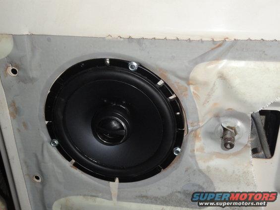 Speaker installed in a white car door panel, showing metal bracing and mounting hardware