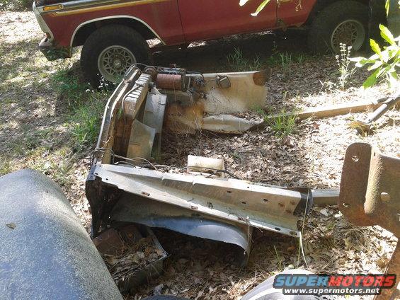 disassembled vehicle front end parts on the ground, red truck in background