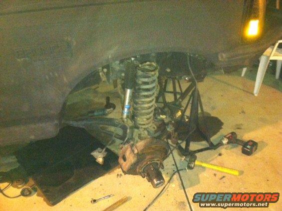 Front suspension of a vehicle is disassembled, with parts on the ground and a coil spring supported by a stand