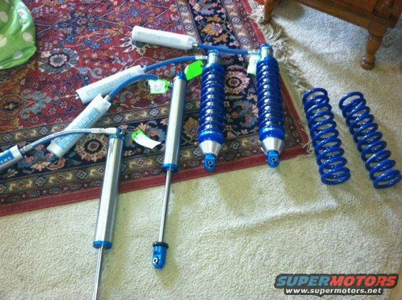 Several blue coilover shocks and separate blue springs laid out on a rug