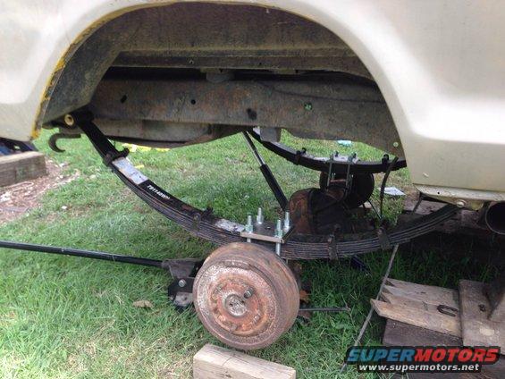 Rear leaf springs and axle assembly of a vehicle, with a jack supporting the axle. The drum brake is visible