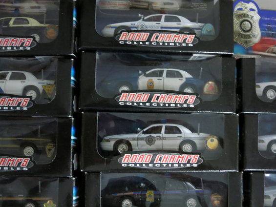 Police car models in boxes, some with "Road Champs Collectibles" branding. A 1992 Ford Crown Victoria is visible