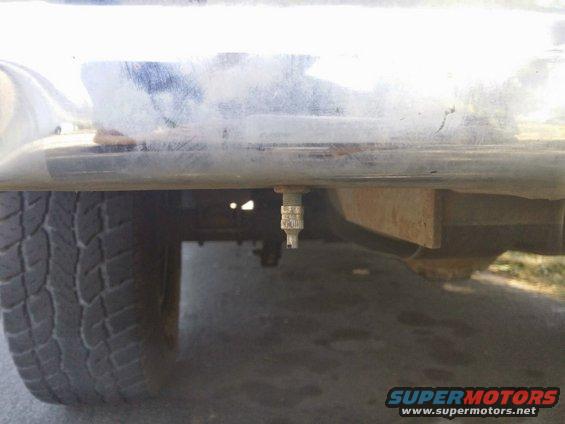 Close-up of a tire valve stem hanging below a chrome bumper