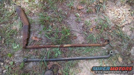 Rusted exhaust pipe section and two metal linkage rods laid on the ground