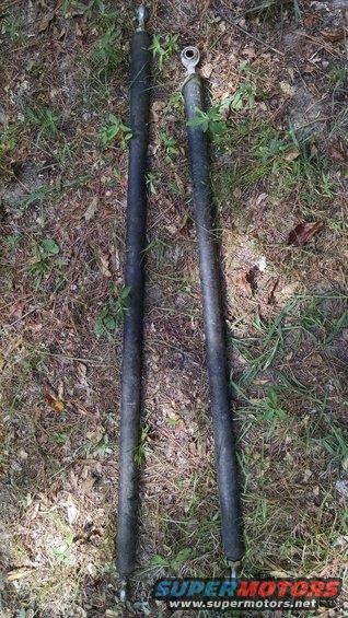 Two black shock absorbers with metal ends lying on the ground
