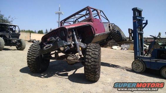 Modified Jeep CJ with roll cage, lifted suspension, and large tires, being lifted by a forklift. Another modified Jeep is visible to the left