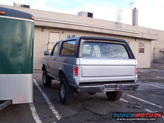 Rear view of a silver 1990 Ford Bronco parked next to a green trailer