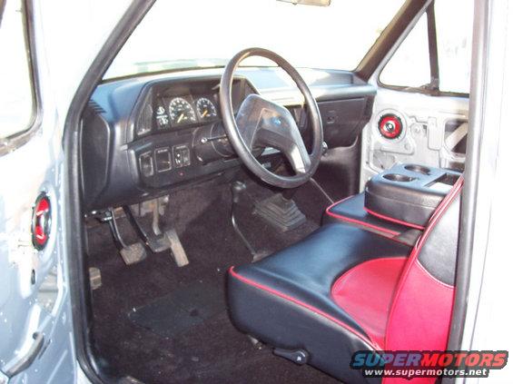 Interior of a truck cab, showing dashboard, steering wheel, seats with red and black upholstery, and a center console with cup holders