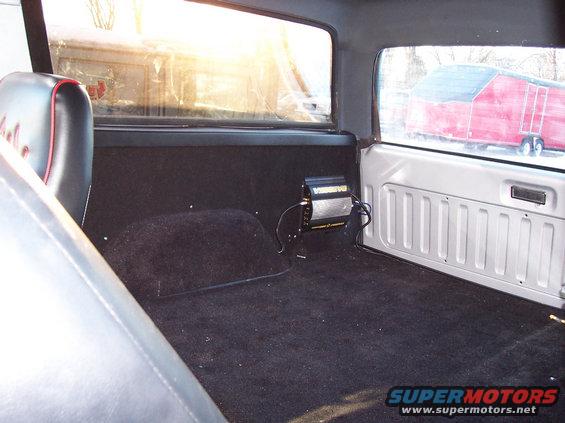 Interior of a 1990 Ford Bronco, black carpet, black seats with red trim, amplifier mounted on the wall
