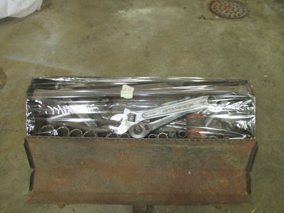 Metal tool organizer filled with wrenches and sockets, covered in plastic wrap