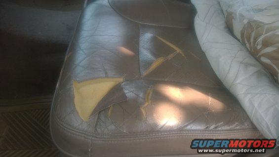 Torn brown leather car seat with yellow foam showing through. A blanket is draped over the seat
