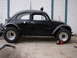 1964 Volkswagen Beetle - A modified black Volkswagen Beetle sits parked in front of a garage door, equipped with off-road tires.