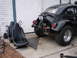 1964 Volkswagen Beetle - A custom black Volkswagen Beetle is shown from the rear, an exposed engine and large off-road tires, with racing seats nearby.