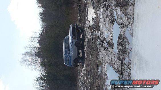 Light blue 1978 Ford Bronco with blue stripe, stuck in mud, side view