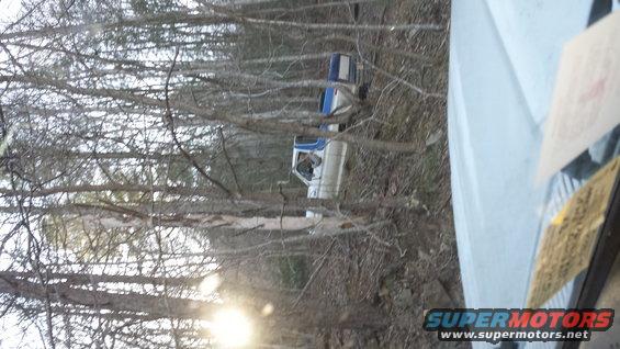 two pickup trucks parked on a wooded trail, one white and blue, the other white