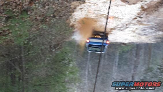 Blue SUV being pulled up a muddy incline by a cable, rear view