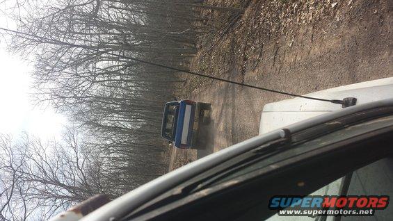 Blue pickup truck driving away on a dirt road, seen from another vehicle