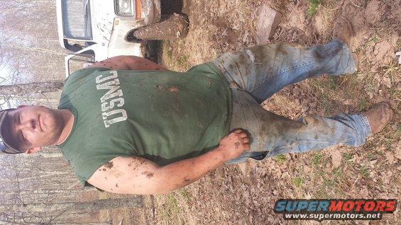 Guy in USMC shirt and jeans covered in mud, lying on the ground next to a white truck stuck in the mud