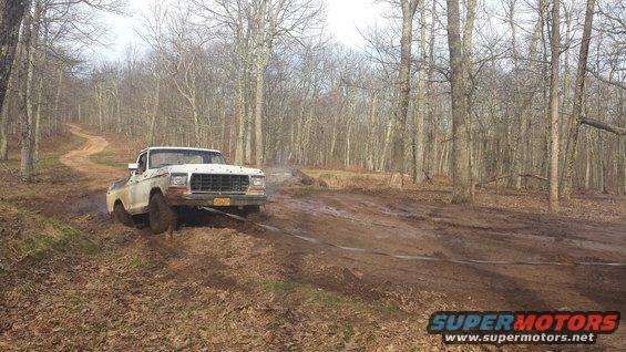 White pickup truck stuck in mud on a dirt road in a wooded area