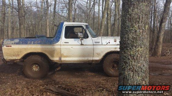 White and blue Ford Bronco with large tires on a muddy trail