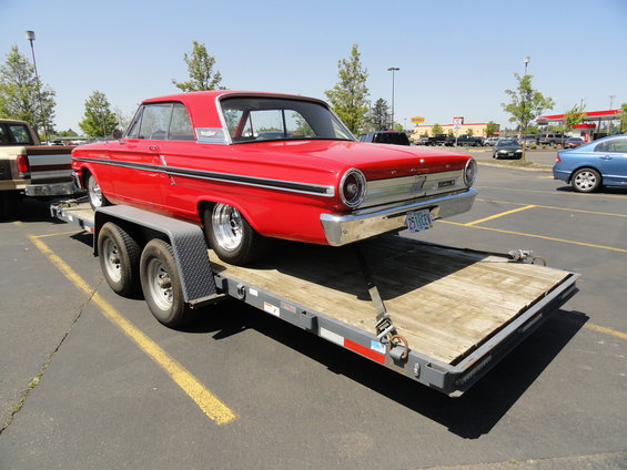Red 1964 Ford Fairlane coupe on a dual-axle trailer, viewed from the front-right