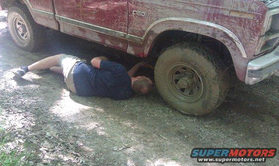 Guy lying on ground fixing red pickup truck, looks like a 1979 Ford F-150