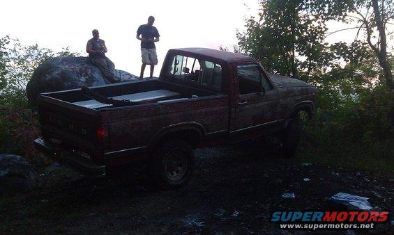 Red pickup truck, weathered, parked on dirt with two men nearby