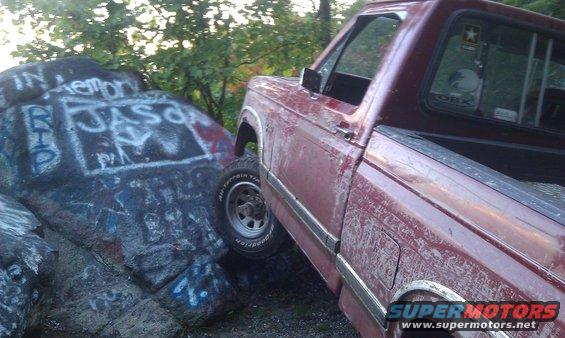 Red pickup truck partially on graffiti-covered rocks