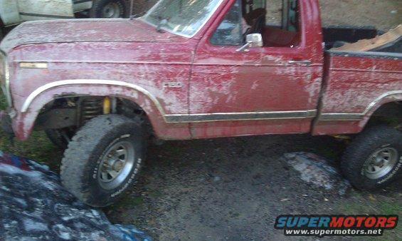 Red pickup truck with "F-150" badge on fender, lifted suspension, off-road tires