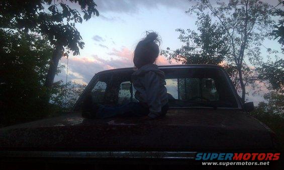 kid sitting on the hood of a pickup truck at dusk