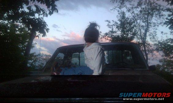 Dark colored truck hood with a person sitting on it, looking at the sky