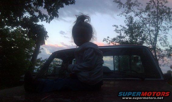 Child sits on hood of old truck at dusk