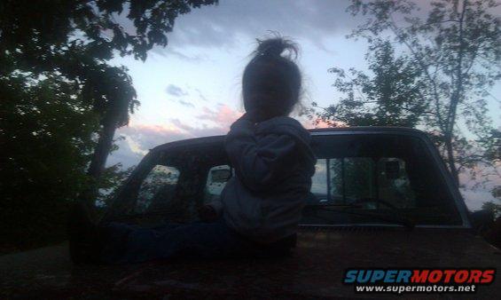 Child sitting on the hood of an old pickup truck at dusk