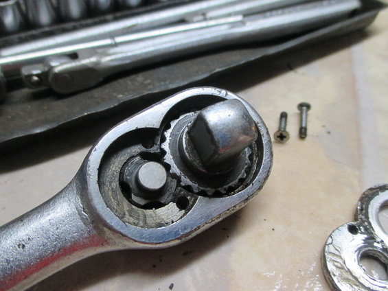 Close-up of a ratchet wrench mechanism with two small screws nearby