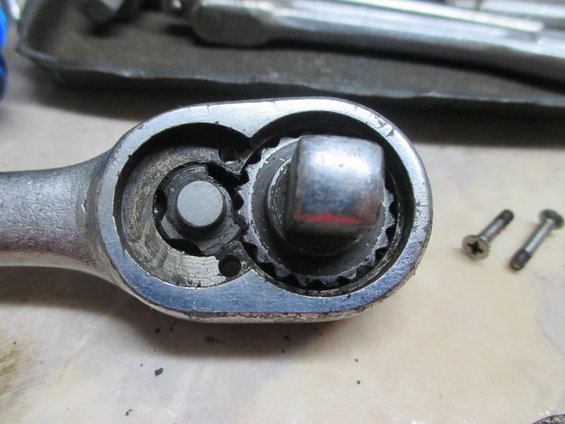 Close-up of a ratchet wrench head showing the internal gears and a square drive. Two small screws are visible to the right