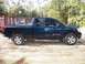 2006 Nissan Titan - A blue pickup truck is parked outdoors with a shipping container in the background. The truck has V8 Titan badging on its side.