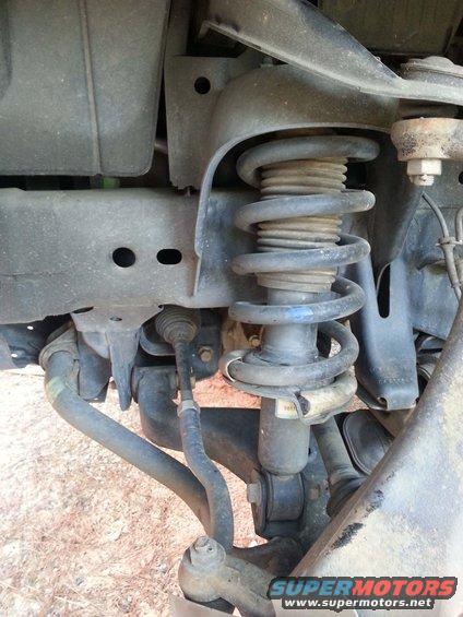 Close-up of a vehicle's front suspension system, showing the coil spring, strut, and control arms
