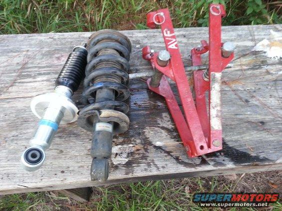 Two struts and a red spring compressor tool on a wooden surface